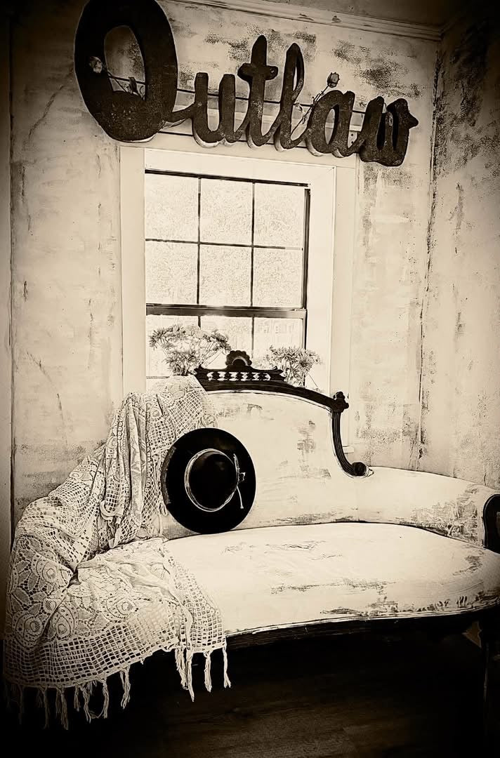 A vintage settee with a lace throw and black hat beneath an Outlaw sign